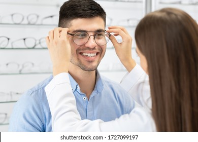 Optical Shop. Female optician in white coat helping handsome guy to buy eyeglasses, selective focus
