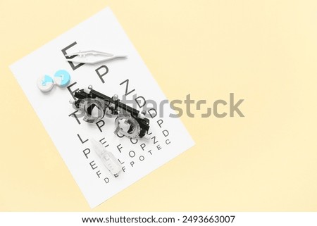 Optical trial frame with eye test chart, container of contact lenses and tweezers on yellow background