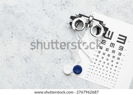 Optical trial frame with eye test chart and set for contact lenses on white grunge background