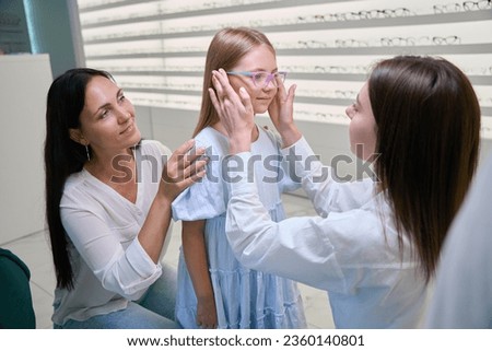 Optician assisting little girl in choosing new pair of spectacles
