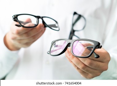 Optician comparing lenses or showing customer different options in spectacles. Eye doctor showing new glasses. Professional optometrist in white coat with many eyeglasses.