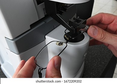 Optician hands adjusting eyeglasses during measurement of dioptry with modern digital lens meter. 