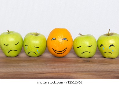 Optimist zwischen Pessimisten und guter Laune Konzept, Äpfel mit gezeichnet traurigen Gesichtern und eine Orange mit einem Lächeln. 