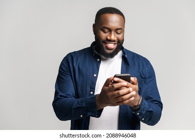 Optimistic African-American man wearing casual shirt texting on the smartphone, texting, smiling black guy enjoying using new mobile app isolated on grey - Powered by Shutterstock