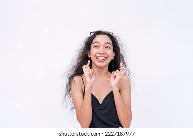 An Optimistic Asian Woman Crosses Her Fingers While Looking Up, Certain About Her Good Luck. Isolated On A White Background.