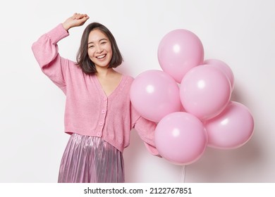 Optimistic Asian woman dances carefree gets balloons as gift wears festive clothes enjoys birthday celebration expresses positive emotions isolated over white background. People fun holidays - Powered by Shutterstock