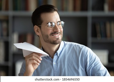 Optimistic businessman in glasses looking away having fun in office folded paper into plane and launching, symbol of creativity at work, daydreaming about future vacation, career aspirations concept