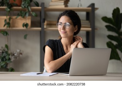 Optimistic dream. Smiling latina female employee sit at workplace distracted from office laptop screen relax visualize future career growth. Young woman enterpreneur thinking on good business decision