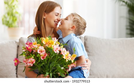 Optimistic family: mother with bouquet of  alstroemeria laughing and touching nose with happy son  during holiday celebration  mothers day at home - Shutterstock ID 1932779513