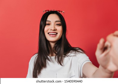 Optimistic girl in white T-shirt smiles and takes selfie on isolated background - Powered by Shutterstock