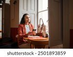 Optimistic Latina entrepreneur working remotely in café. Businesswoman smiling with phone and laptop, enjoying a productive day