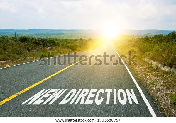 Optimistic road landscape with sunlight ahead and New\
Direction inscription. Motivational inscription on the road going\
forward. The beginning of a new path. A conceptual photo of the\
path. 