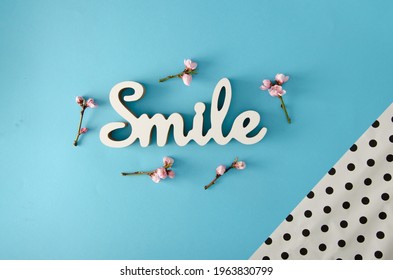 Optimistic spring arraignment. Smile sign and pink flowers on a pastel blue background. Minimal creative flat lay.