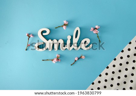 Optimistic spring arraignment. Smile sign and pink flowers on a pastel blue background. Minimal creative flat lay.