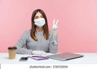 Optimistic woman employee sitting safe healthy with protective mask and gloves during quarantine, showing victory, peace gesture. Working at home office in self-isolation, coronavirus outbreak. indoor