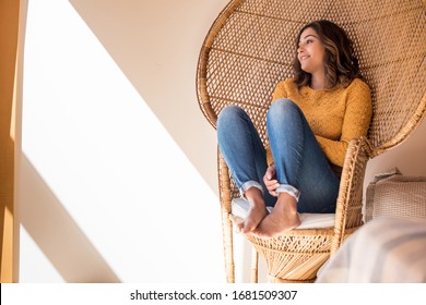 Optimistic woman sitting in a confortable rattan chair at home
