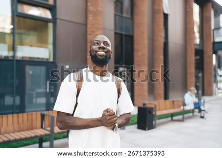Optimistic young man in white looking upward with hopeful smile, symbolizing inspiration, digital possibility, and connection in technology-driven modern lifestyle.