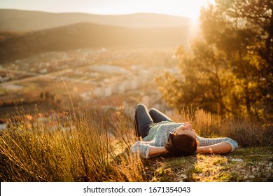 Optimistic Young Woman Listening To Music Podcast Stream Over Headphones,enjoying In Nature At Sunset.Musical Therapy.Day In Nature.Mindfulness Guided Meditation.Stress Menagement.Idea Inspiration.