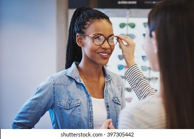 Optometrist Fitting Glasses On An Attractive African American Woman Customer Inside A Store As She Selects A Frame