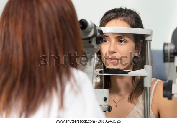 Optometrist woman examining the eyesight of another\
woman with a slit\
lamp