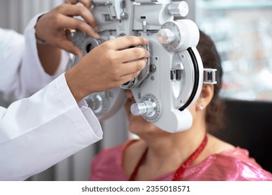 Optometrist's hand adjusting Phoropter for middle-aged Indian or Nepalese woman during eye examination, diagnostic ophthalmology  - Powered by Shutterstock