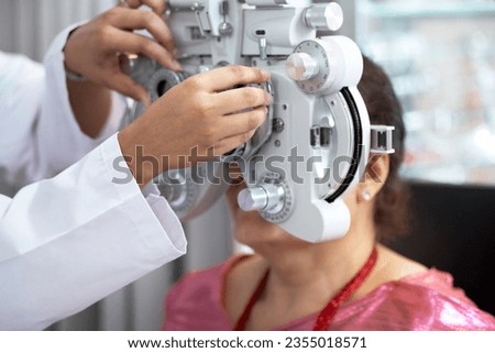 Optometrist's hand adjusting Phoropter for middle-aged Indian or Nepalese woman during eye examination, diagnostic ophthalmology 