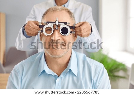 Optometry specialist doing eye test during checkup consultation visit. Optometrist or ophthalmologist uses phoropter ocular device tool to measure vision diopters of mature man with retina defects