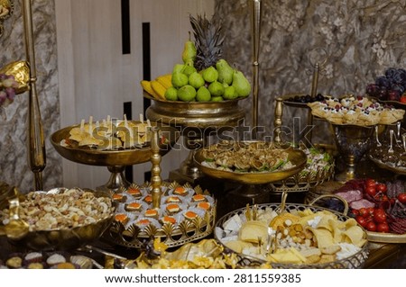 An opulent buffet table setup featuring assorted gourmet appetizers, a large cheese and charcuterie platter, nuts, fresh fruits, and desserts, set on
