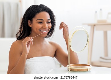 Oral Care. Smiling Black Woman Looking In Mirror And Using Dental Floss In Bathroom, Attractive Young African American Female Cleansing Teeth, Making Morning Hygiene At Home, Closeup Shot