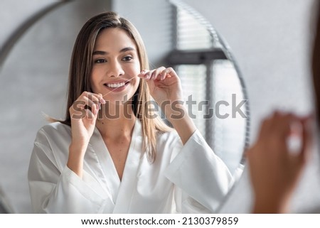 Oral Care. Smiling Young Female Using Dental Floss Near Mirror In Bathroom, Beautiful Millennial Woman Cleansing Teeth, Making Daily Hygiene Routine At Home, Seletive Focus On Reflection