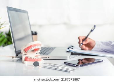 Oral Dental. Dentist Doctor In Uniform Writing Information Of Patient In Paperwork Checklist On Clipboard On Desk Office, Teeth Model, X-ray On Laptop Screen, Prescription Medical Dental Healthcare