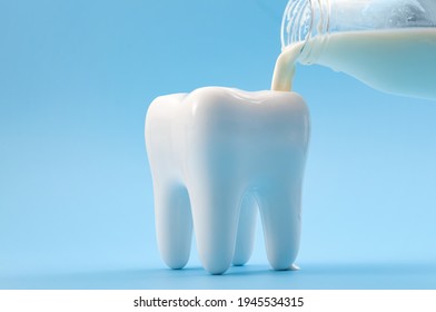 Oral health, cavity prevention and calcium rich drink for strong teeth concept with glass bottle pouring milk into a heathy tooth isolated on blue background - Shutterstock ID 1945534315