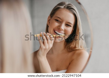 Oral hygiene, healthy teeth and care. Young woman brushing teeth with toothbrush and looking in mirror in bathroom interior in the morning, closeup, empty space