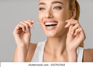 Oral hygiene. Young woman with perfect smile using dental floss, grey studio background - Shutterstock ID 1557917654