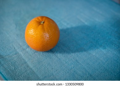 An orange against a blue background, daylight shining in.
