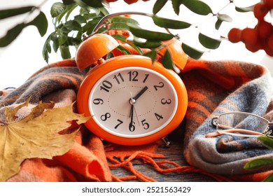    Orange alarm clock in a warm checkered blanket, flowers nearby - autumn time                            