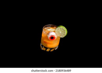 Orange alcoholic cocktail with an artificial jelly eye, decorated with lime on a black background.