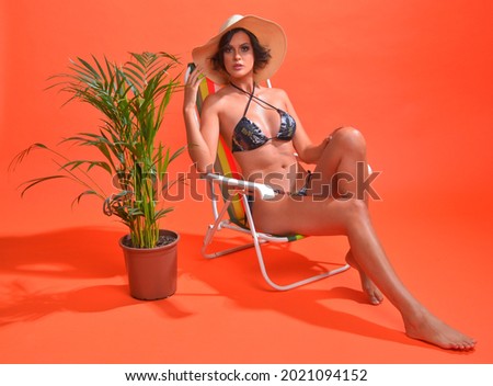 orange background, photo shoot in studio, bikini and beach hat.