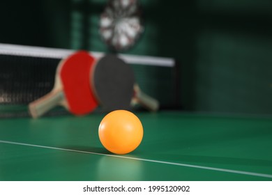 Orange ball on green ping pong table indoors. Space for text