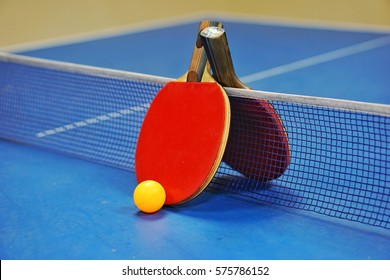 Orange Ball With A Table Tennis Racket Red And Black On A Blue Table With Blurred Background, Indoor Games