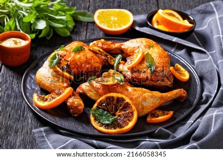 Orange Barbecue Grilled Chicken on black plate with sage and dijon mustard on dark wooden background, horizontal view from above, close-up