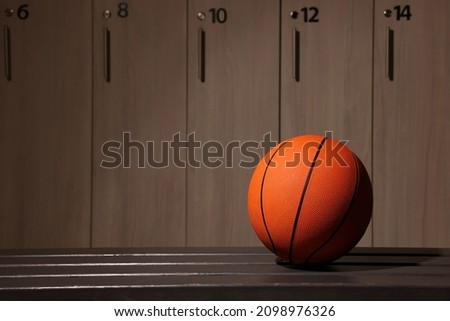Orange basketball ball on wooden bench in locker room. Space for text