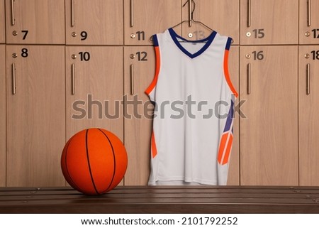 Orange basketball ball on wooden bench and hanger with uniform in locker room