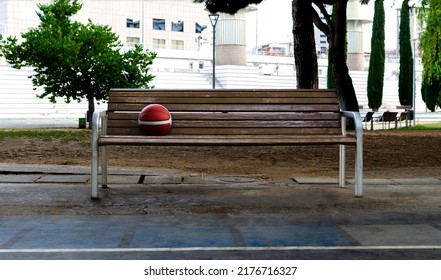 Orange Basketball On A Bench In A Public Park Next To The Court. No People Around. Concept Of Time-out, Rest Time.