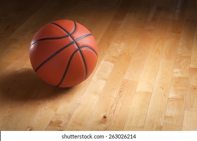 An Orange Basketball Sits On A Hardwood Court Floor With Spot Lighting And Background That Goes From Dark To Light.