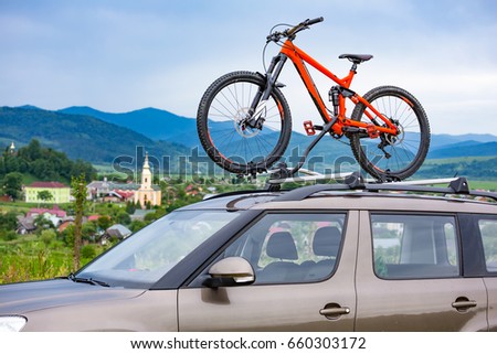 Orange bicycle mounted to the roof of a car on the background of beautiful mountain landscape