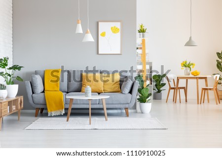 Orange blanket on grey sofa in modern apartment interior with poster and wooden table. Real photo