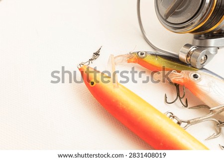 Orange and blue artificial baits with sharp treble hooks resting near a fishing reel
