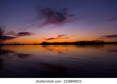  Orange, Blue And Purple Sunset On River With Dark Colorful Clouds In Sky With Trees Reflection In Water