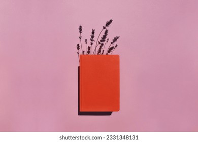 Orange book or notebook with lavender flowers inside on pink background with long shadows. Banner. Space for text. Copy space. Knowledge day. Back to school concept. Time to study